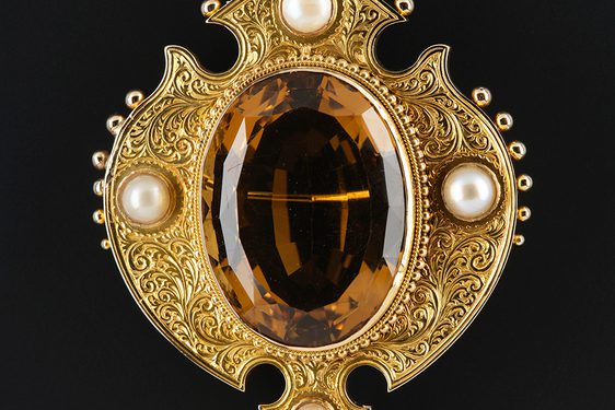 A gold brooch featuring a large oval cairngorm stone, surrounded by four pearls.