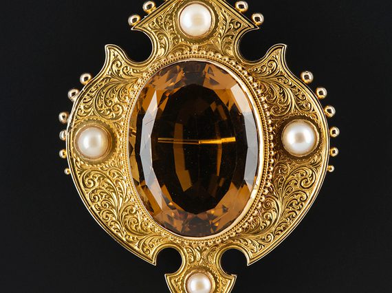A gold brooch featuring a large oval cairngorm stone, surrounded by four pearls.