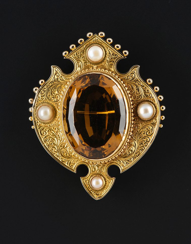 A gold brooch featuring a large oval cairngorm stone, surrounded by four pearls.