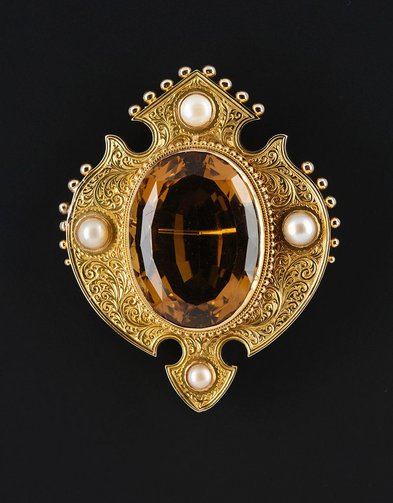A gold brooch featuring a large oval cairngorm stone, surrounded by four pearls.