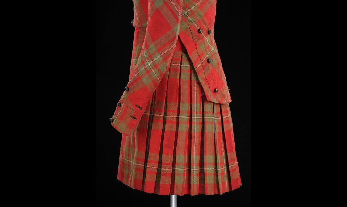 Detail of a mannequin wearing a red tartan kilt with a matching jacket.