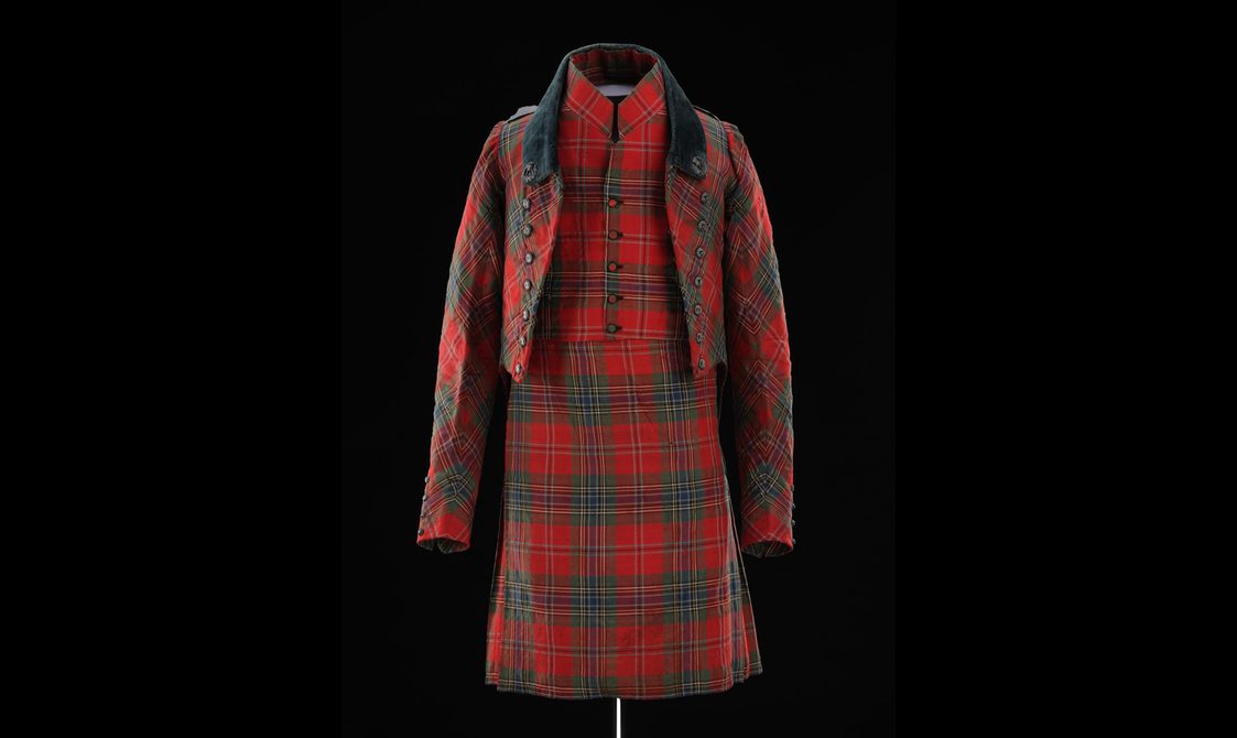 A mannequin wearing a red tartan kilt with matching waistcoat and short jacket.