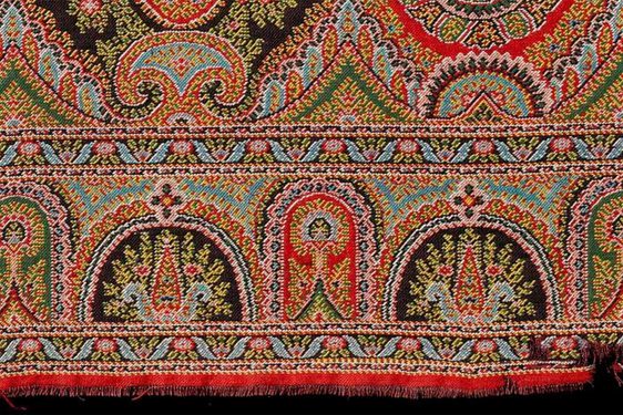 Paisley shawl pattern, short length of a woven border with long cone or buta shapes at the centre, detailed multi-coloured design predominantly in shades of red, blue and green.