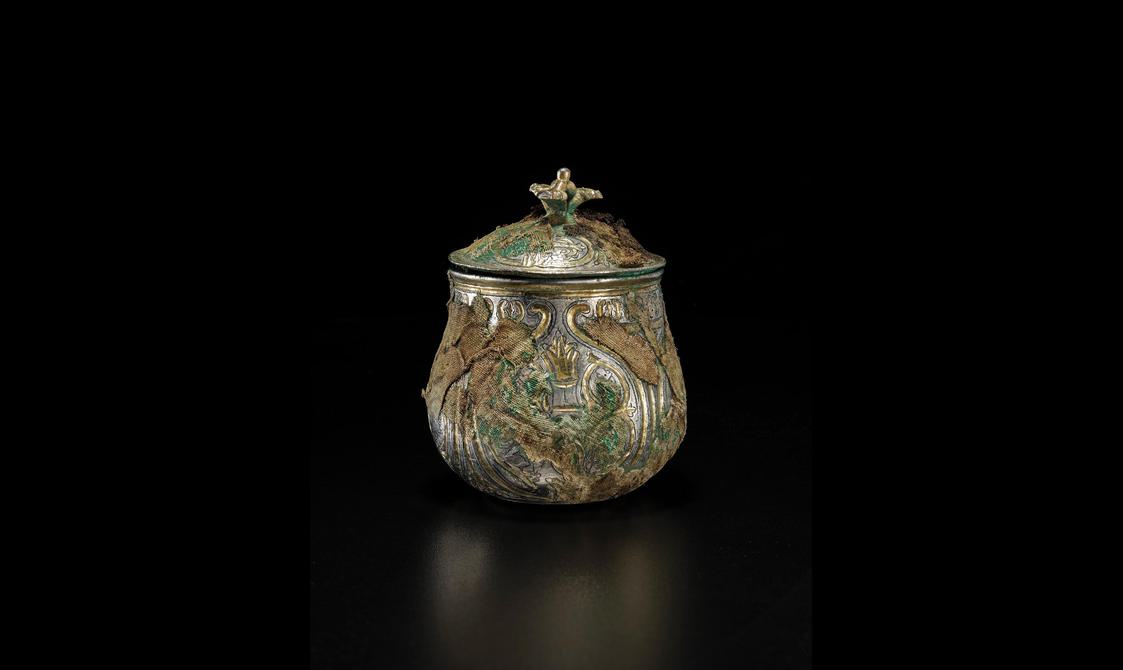 A silver round vessel with a gilded lid engraved with various round and organic shapes
