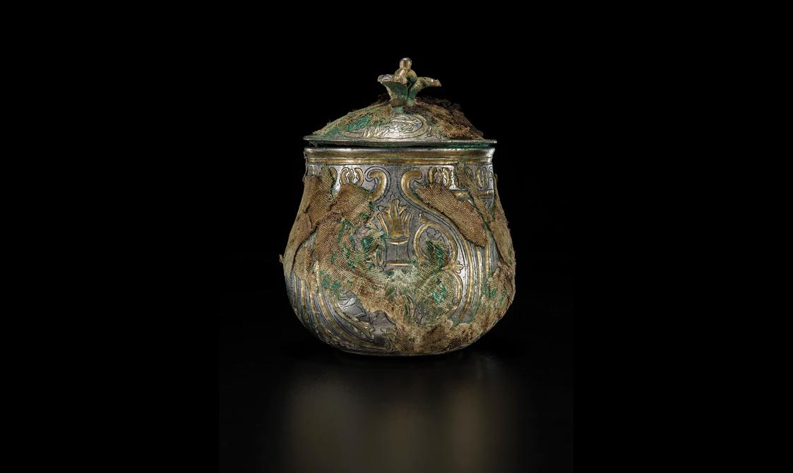 A silver round vessel with a gilded lid engraved with various round and organic shapes