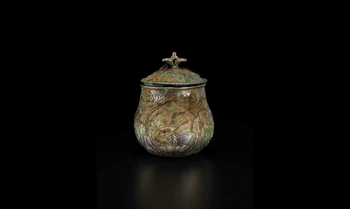 A silver round vessel with a gilded lid engraved with various round and organic shapes.