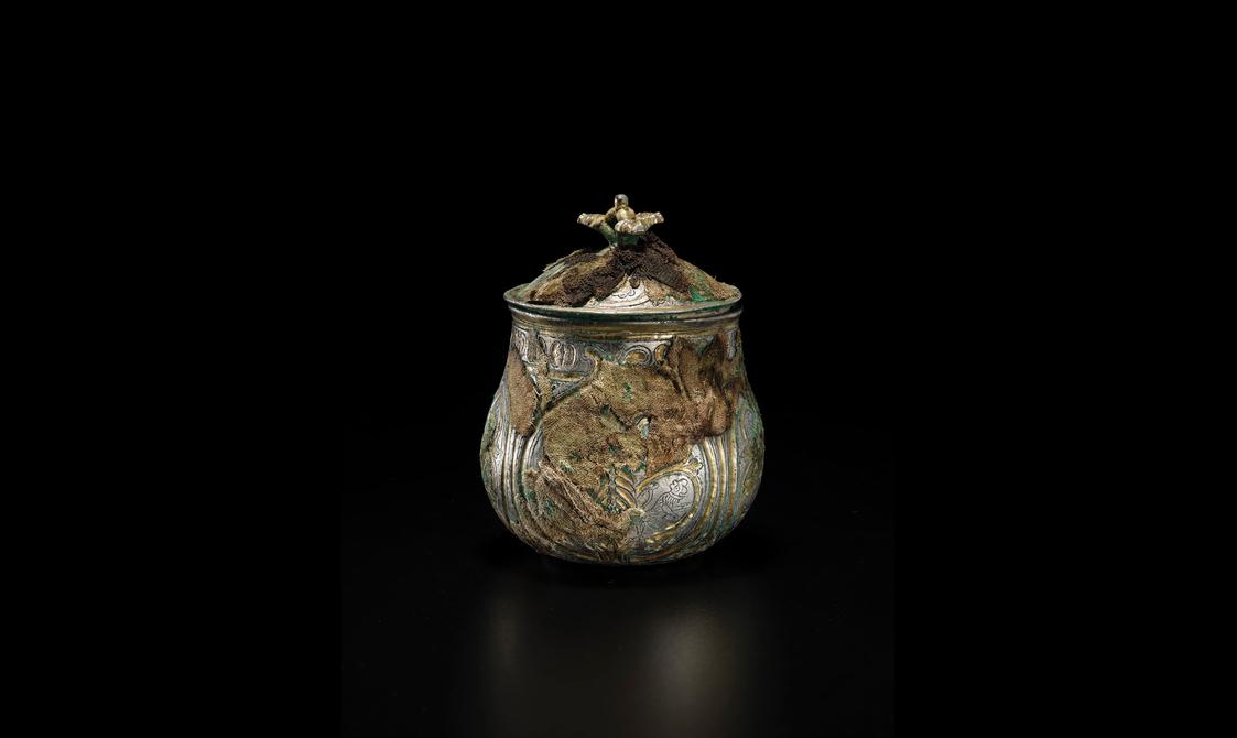 A silver round vessel with a gilded lid engraved with various round and organic shapes