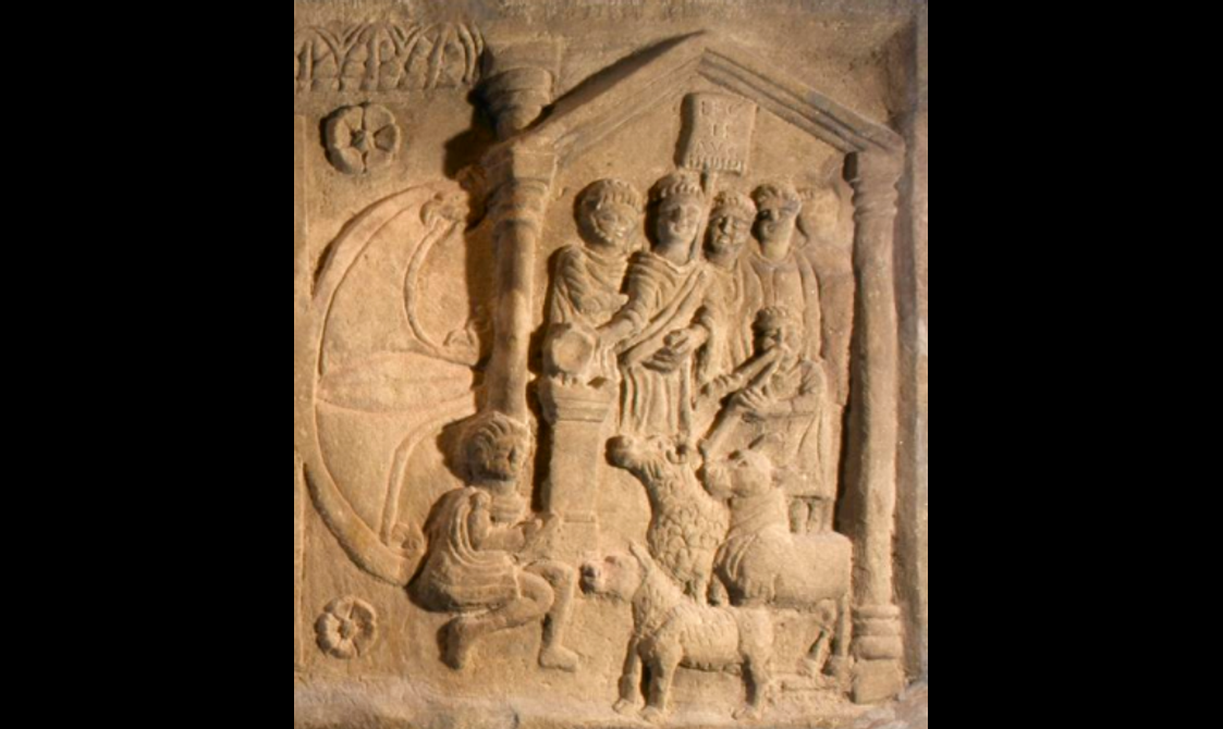 Close-up of a detailed carving of several people and livestock animals gathered around a small altar. One person plays a flute.