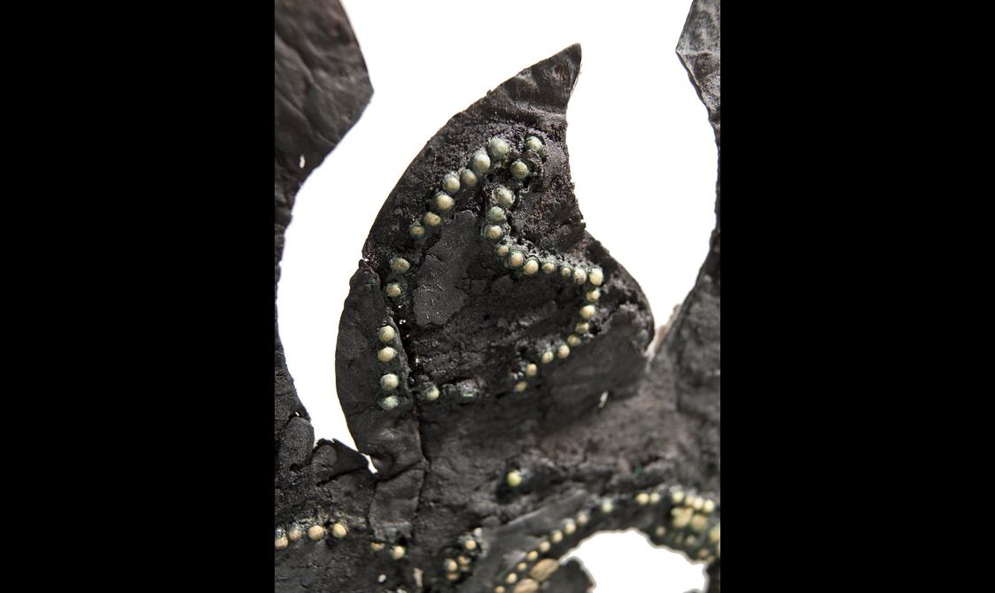 Extreme close-up of the triangular earpiece section. Blackened, cracked leather decorated by a bronze circle and many studs, some missing.
