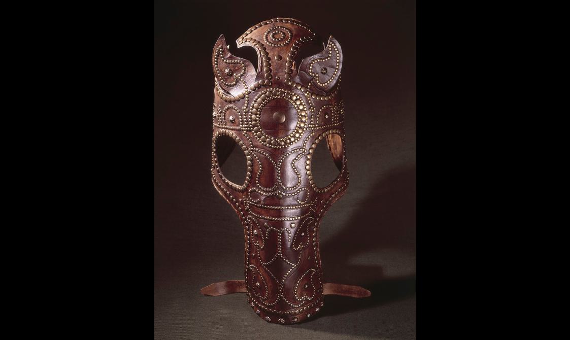 Reddish-brown, obviously new and prestigious leather helmet in the shape of a horse's head, stood upright and towards the camera as though worn by an approaching horse.