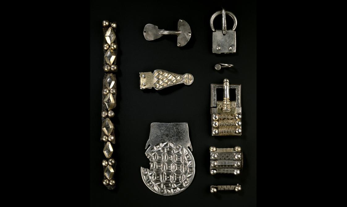To strips of vertically-arranged belt straps flank three buckles of varying shapes, from simple and axe-like to one with a fractal-like silver pattern.