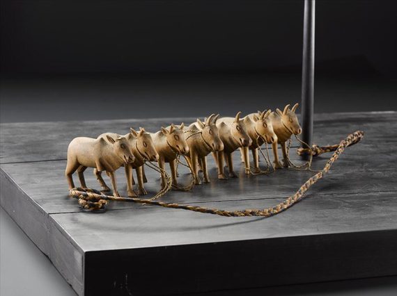 Models of seven oxen standing in a row with rope attaching them to a wooden pole.