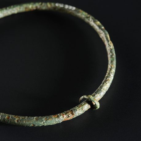 A weathered bronze ring with a small ring attached to it against a black background