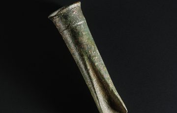A tool made of weathered bronze with a rounded end and a pinched end