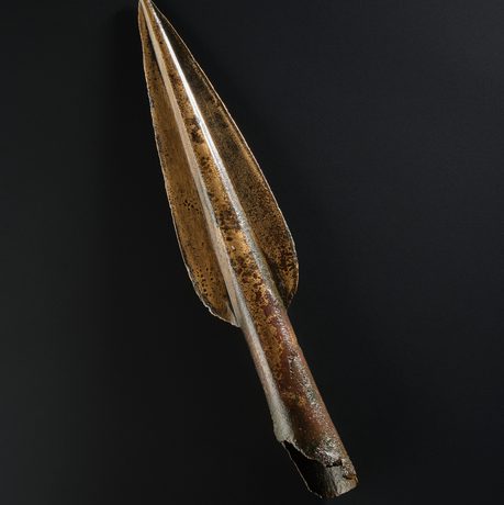 A spearhead bade of bronze against a black background