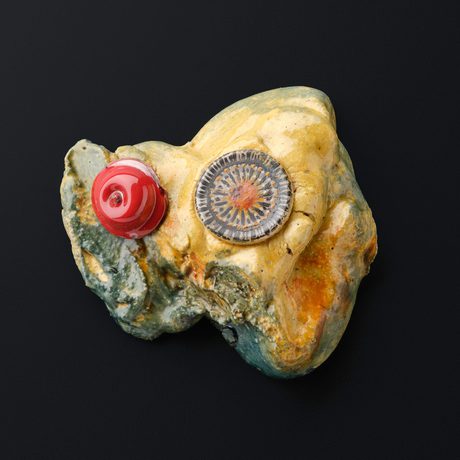 A glass sculpture depicting a yellow and blue marbled rock with a red blob and a grey and orange disk shaped sea creature on top