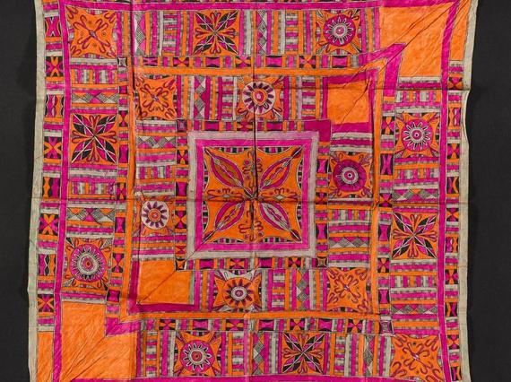 A square piece of pink and orange textile laid flat. It has intricate geometric patterns.