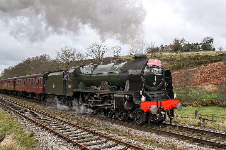 A green and red steam train on a track moving through the countryside.