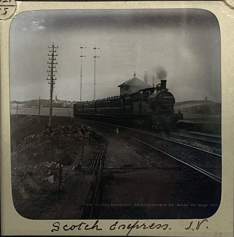 A black and white square slide of a steam train moving on a train track through the countryside.