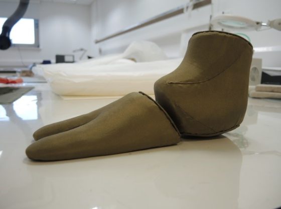 A museum display mount for a sock covered in a dark green textile.