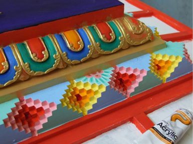 A detail of a wooden object with colourful painted and engraved detailing in red, blue, yellow, and green.