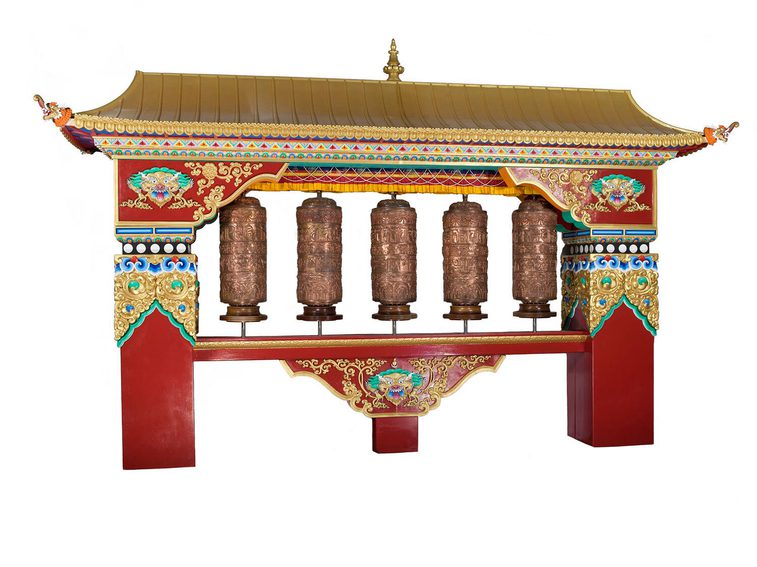 A house like frame with a gold roof and red pillars and decorated surfaces. There are five brown spinning prayer wheels inside.