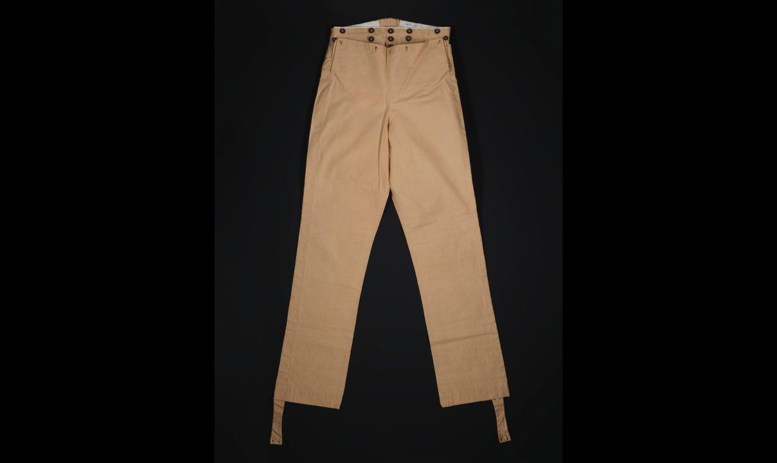 Pair of beige cotton men's trousers with straps hanging at the ankles to go under the foot