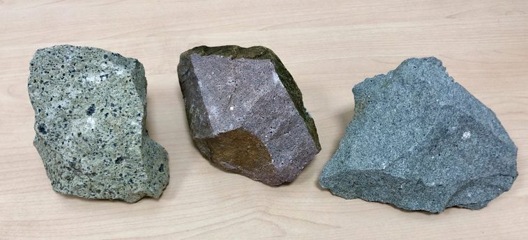 3 small rock samples side by side. The left one is green/grey with black spots, the middle is red, and the right is grey/blue.