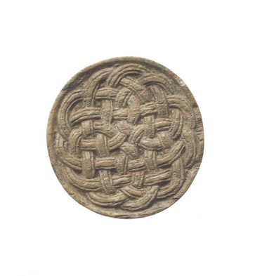A beige stone in the shape of a disk with a knotted celtic pattern