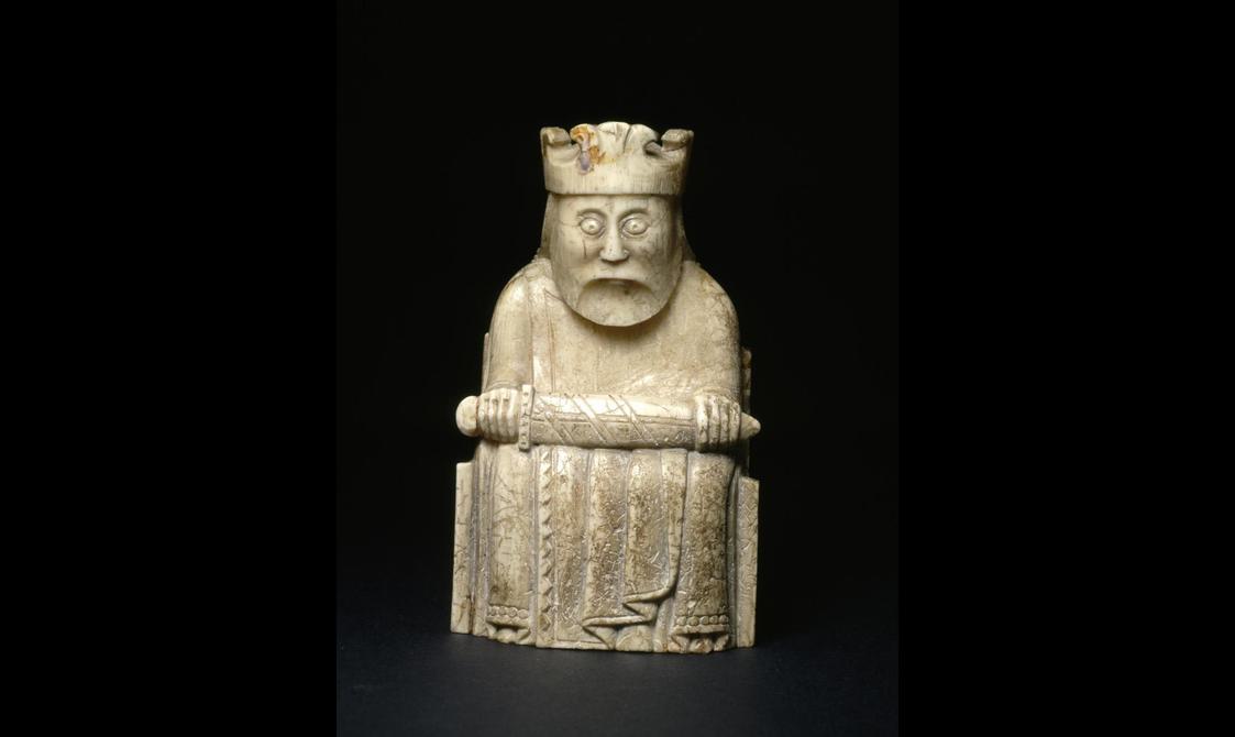 An ivory chess piece of a king seated with a crown on his head with a sword across his lap
