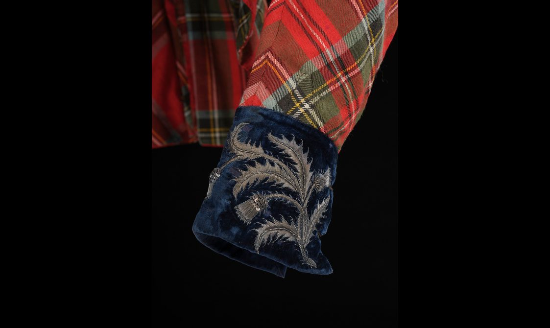 Detail of navy velvet cuffs with silver thistles embroidered on a red tartan jacket.