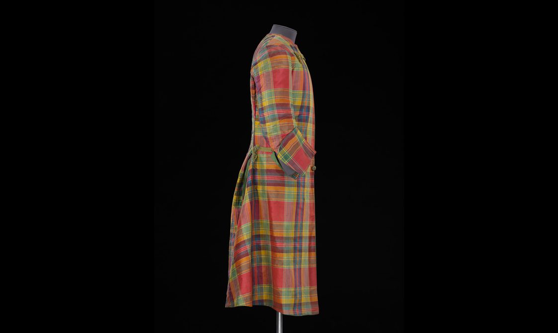 Side view of a mannequin wearing a long red, green, and yellow silk tartan coat