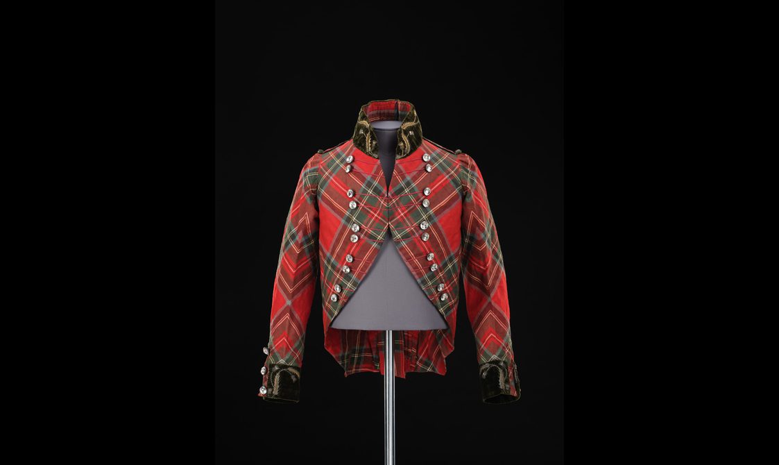 A mannequin wearing a short red tartan jacket with a velvet collar and cut glass buttons.