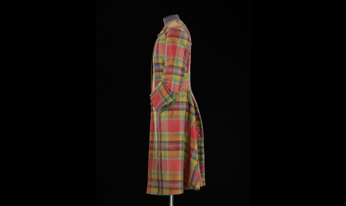 Side view of a mannequin wearing a long red, yellow, and green silk tartan coat