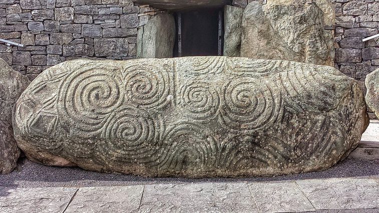 A yellow oval square rock, carved with large spiral and diamond shaped decorations.