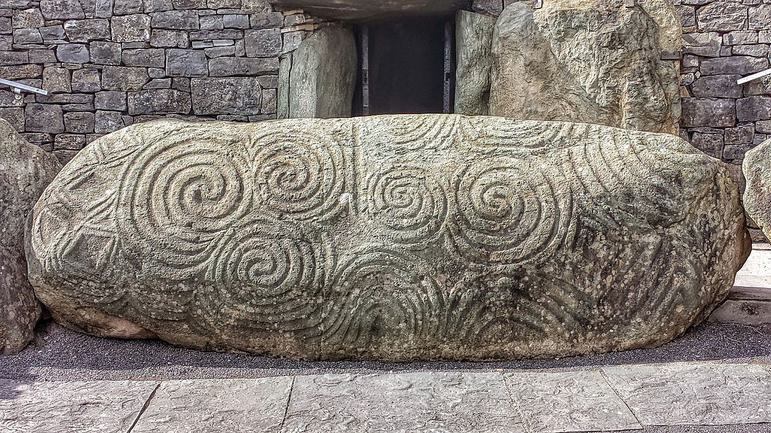 A yellow oval square rock, carved with large spiral and diamond shaped decorations.
