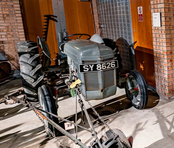 A colour photograph of a TE20 Ferguson tractor. It has 2 large grey rubber tyres at the rear and 2 smaller rubber types at the front and an chevron-shaped grill at the very front.