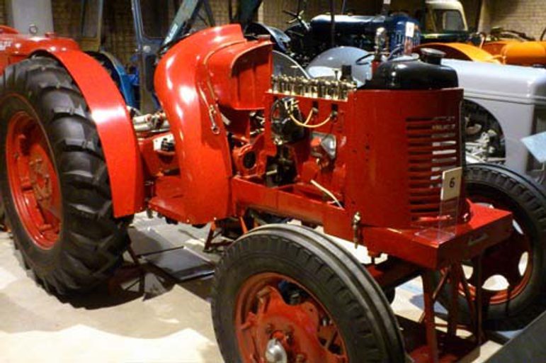 A red compact tractor with 2 large black rubber wheels at the rear and 2 smaller black ridged rubber wheels at the front
