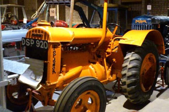 A colour photograph of a large orange tractor with big black rubberised wheels, There is black vertical lettering at the front spelling the word Fordson. It also has a number plate DSP 920