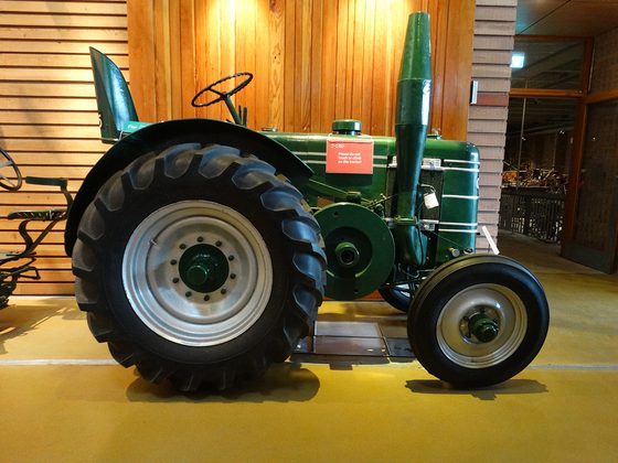 A photograph of a sideview of a dark green tractor. It has a tall chimney and 2 large black rubber tyres at the back and 2 smaller rubber trees at the front.