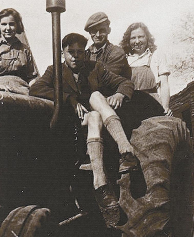 A black and white photograph showing a number of people (2 women, 1 man and a boy) on a tractor during the second world war.