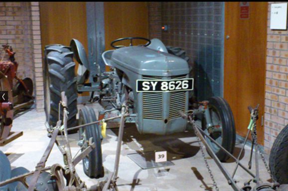 A colour photograph of a TE20 Ferguson tractor. It has 2 large grey rubber tyres at the rear and 2 smaller rubber types at the front and an chevron-shaped grill at the very front.