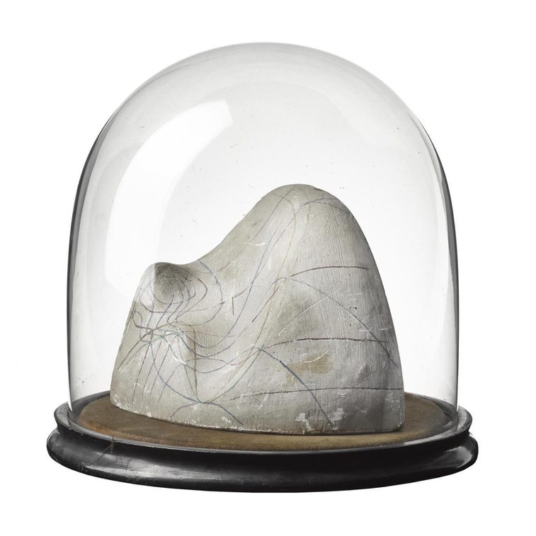 A white plaster cast object with coloured lines on its surface sitting on a wooden disc covered with a glass dome top.