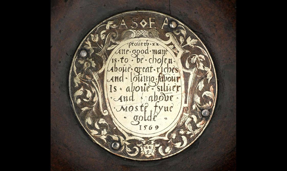 A round plaque with floral detail around the border with text engraved in the middle and the year 1569
