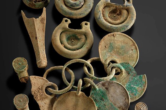 Twelve bronze objects, including some rounded fittings with concentric circle designs and a rattle pendant.