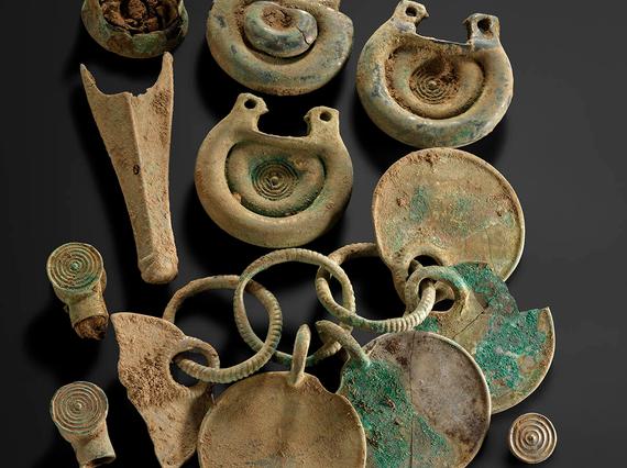 Twelve bronze objects, including some rounded fittings with concentric circle designs and a rattle pendant.