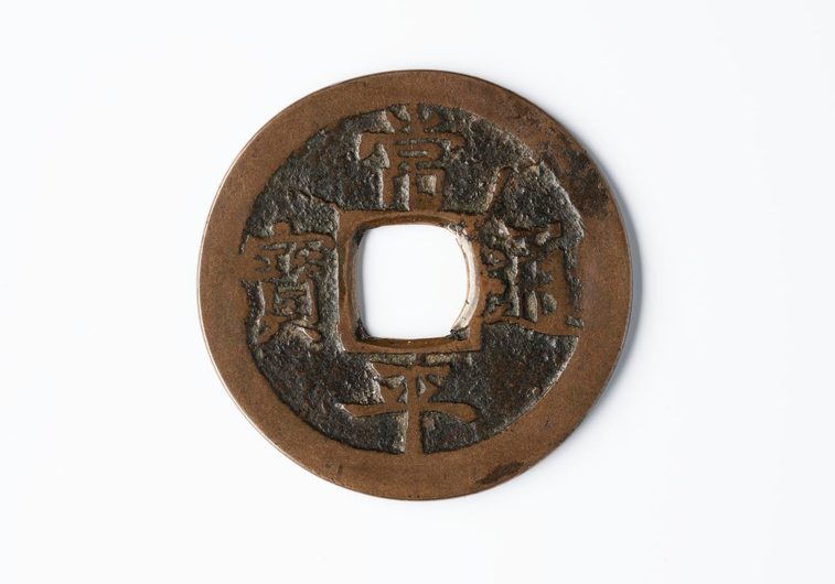 A round brown disc with a hole in the middle and Korean characters engraved on its surface.