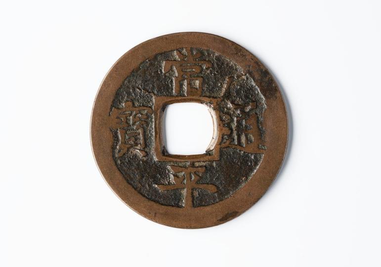 A round brown disc with a hole in the middle and Korean characters engraved on its surface.