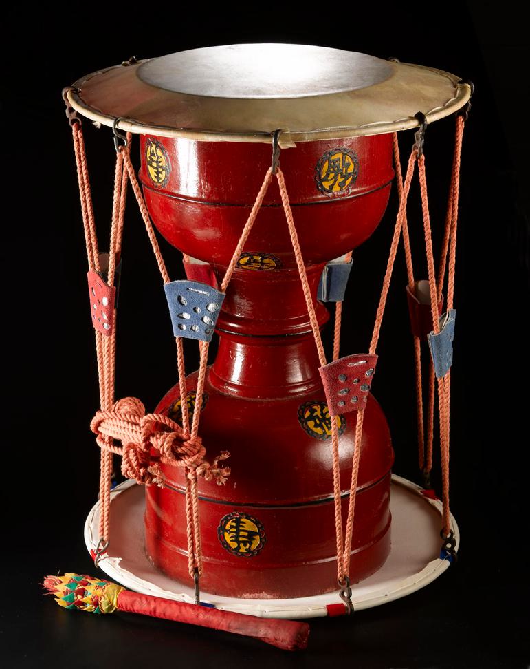 A drum made from red hourglass shaped wood with rope criss crossing from the top to bottom.