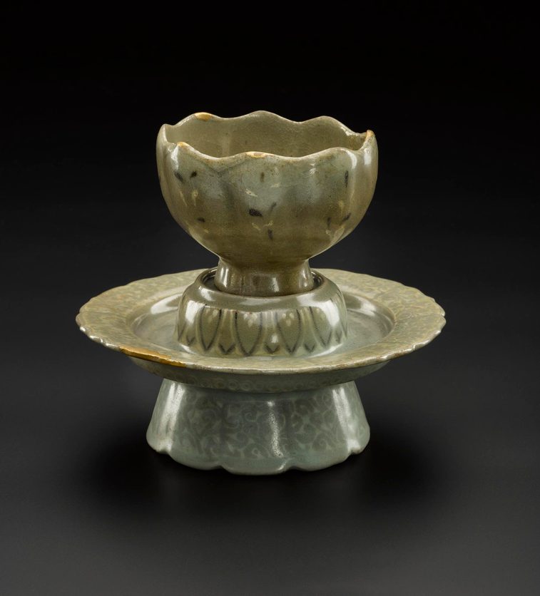 A light green cup made of polished stone sitting on a stand of the same material.